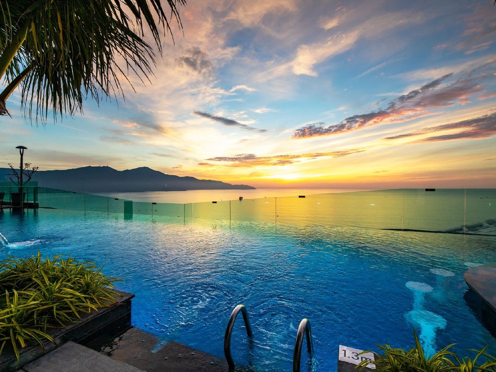 Rooftop infinity pool at sunset, its edge running out toward the sea and the Son Tra peninsula on the horizon