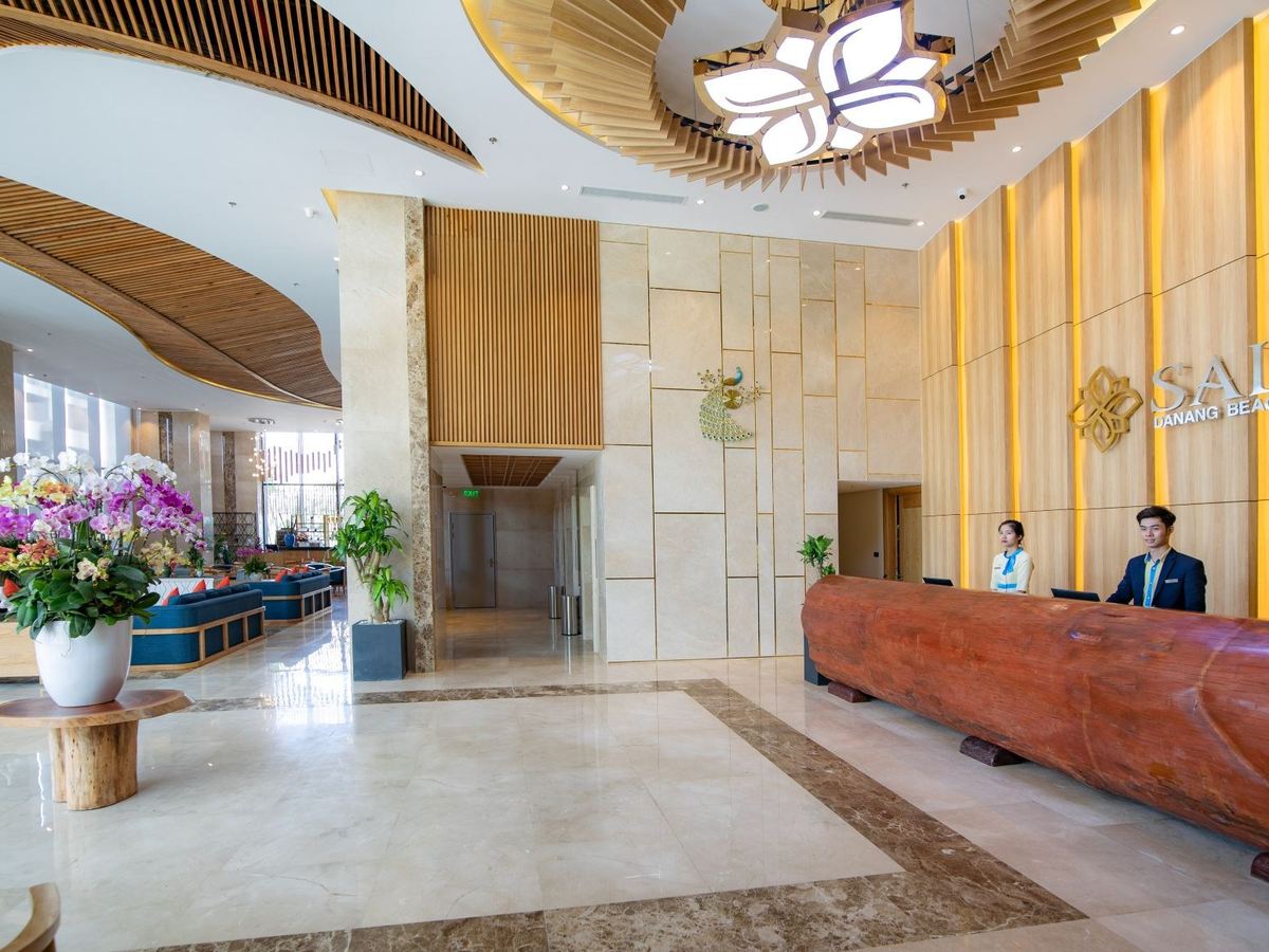 Hotel reception desk in a bright marble lobby with a carved ceiling and orchids