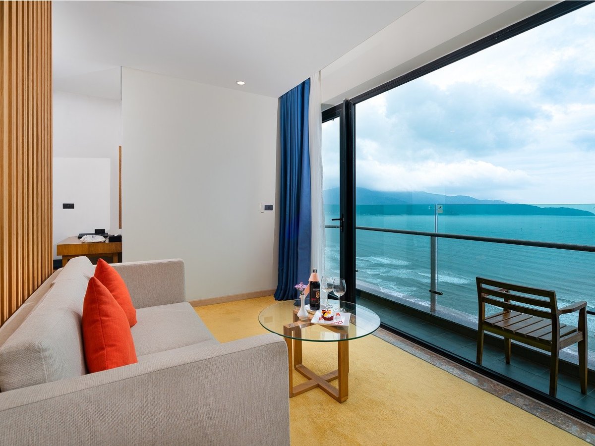 Sea-view balcony seen from a suite, with a sofa, a glass table and a railing over the beach road