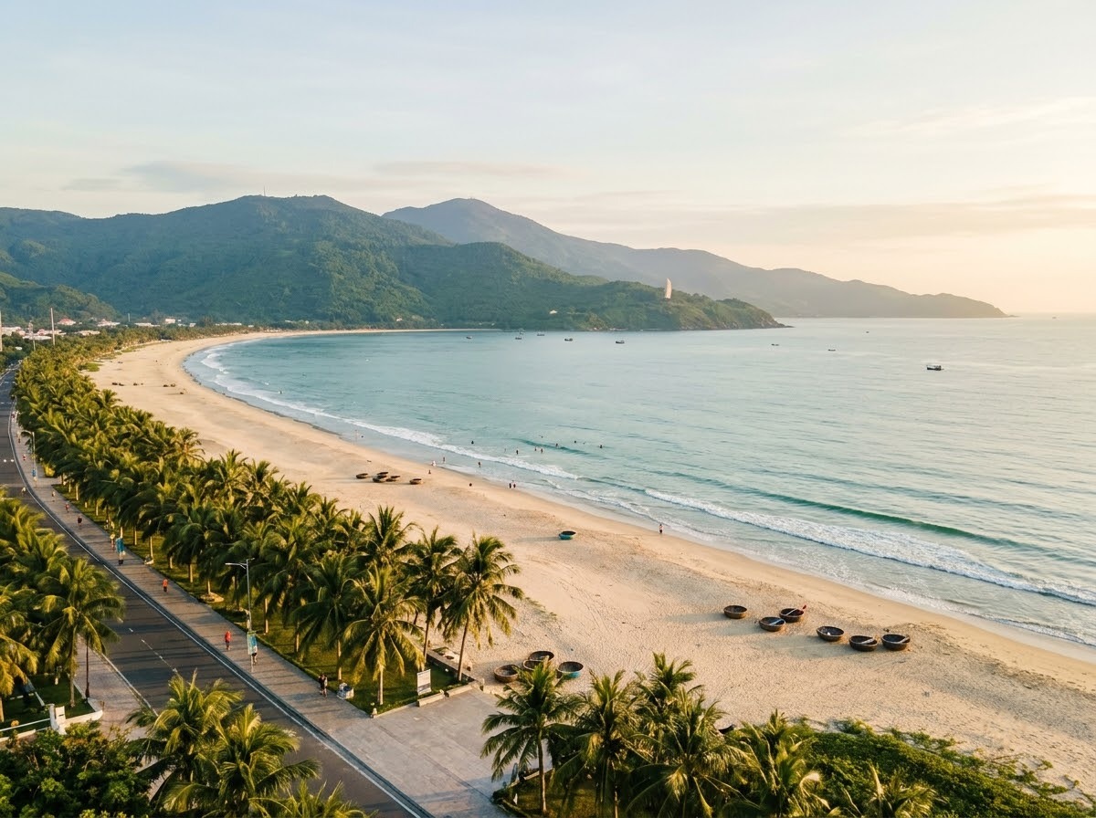 Long curve of My Khe Beach seen from above, with the beach road, palms and the Son Tra peninsula at the far end