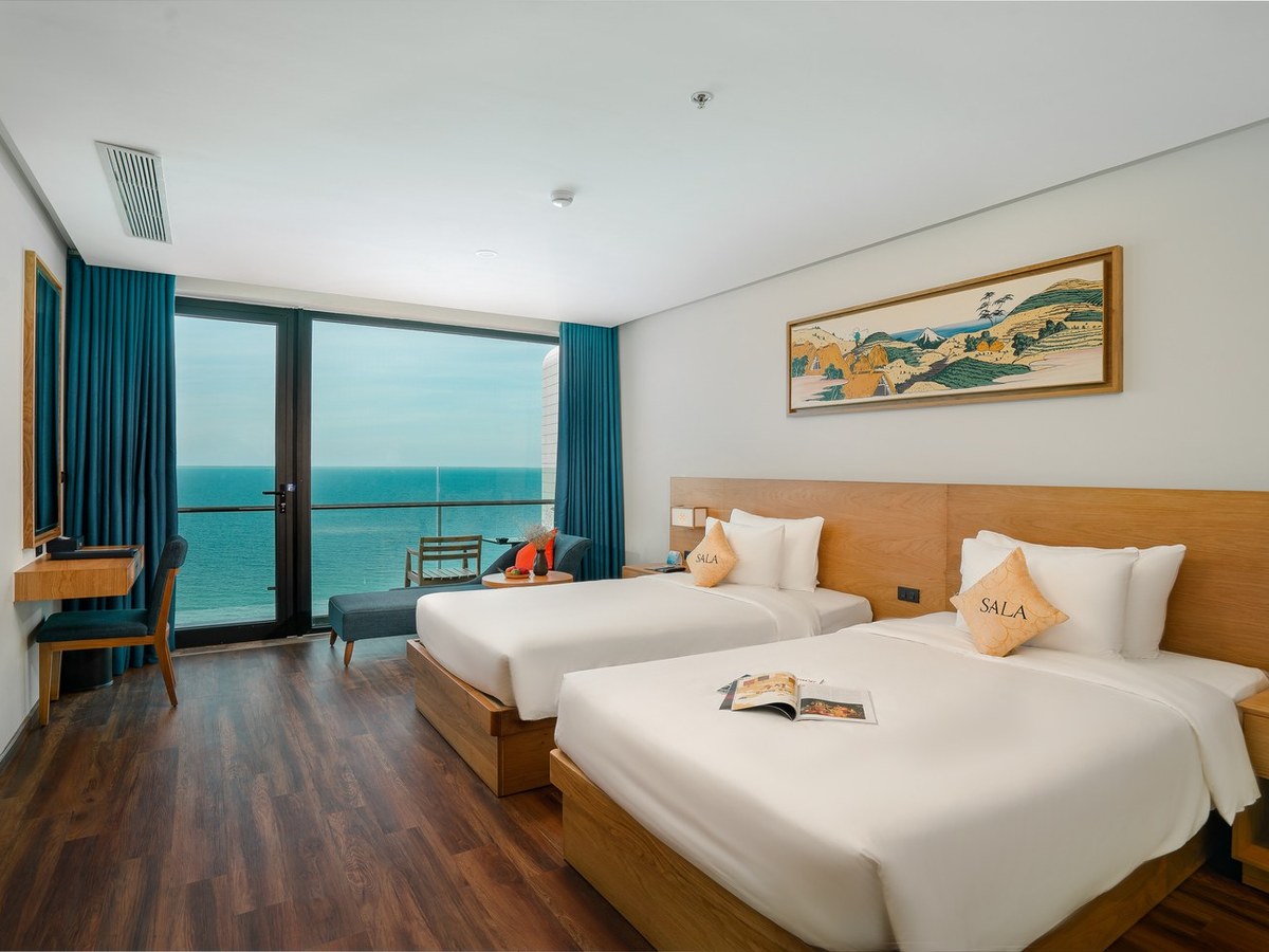 Twin room with two white beds facing a wall of glass onto the sea