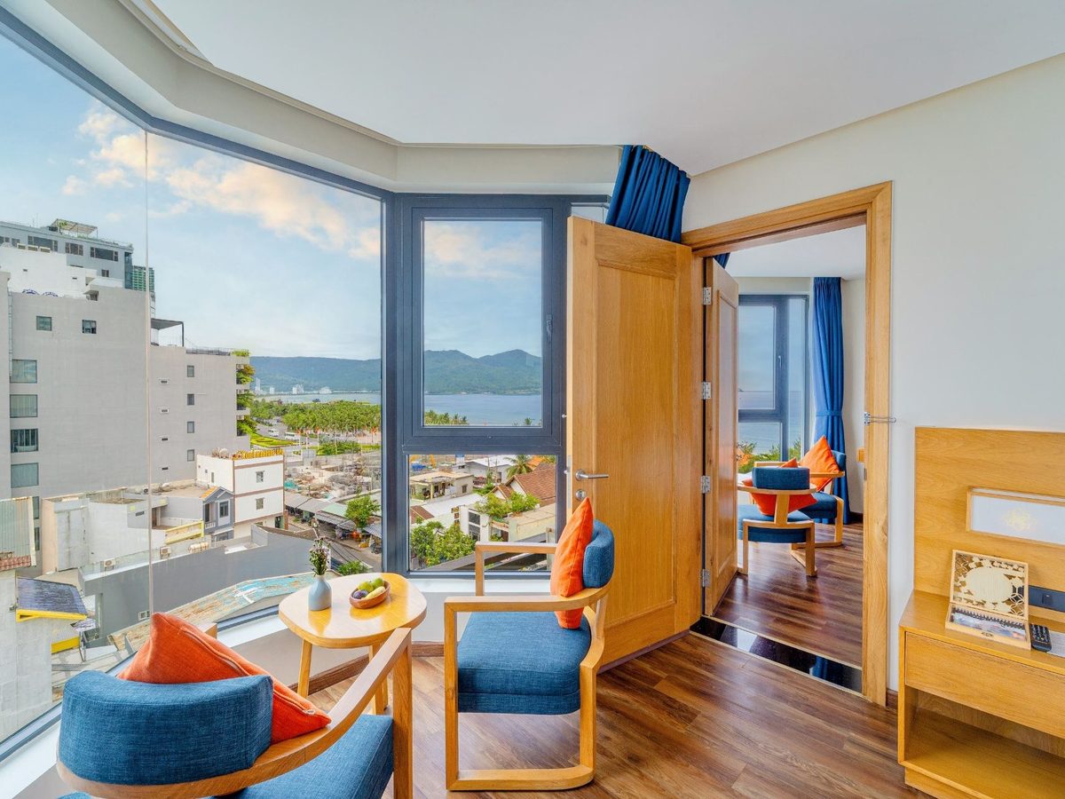 Corner room with blue armchairs by floor-to-ceiling windows looking over rooftops to the sea
