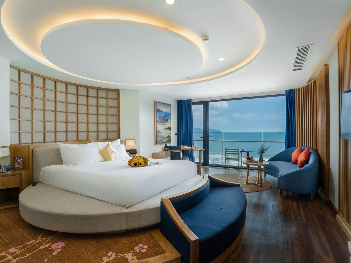Suite with a round bed area under a circular ceiling light and a sofa by a sea-view window