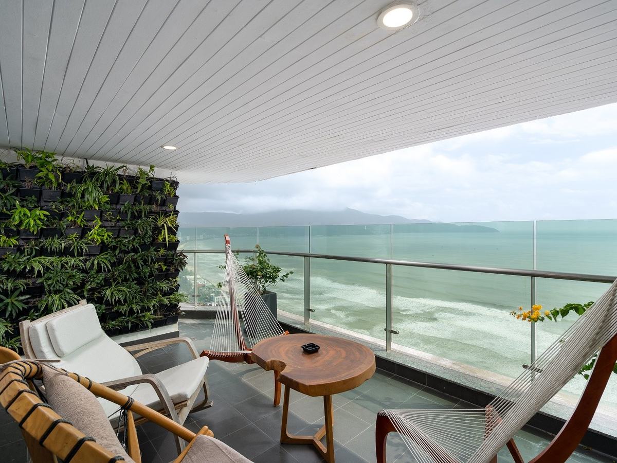 Wide balcony with lounge chairs and a green plant wall above the sea and the beach