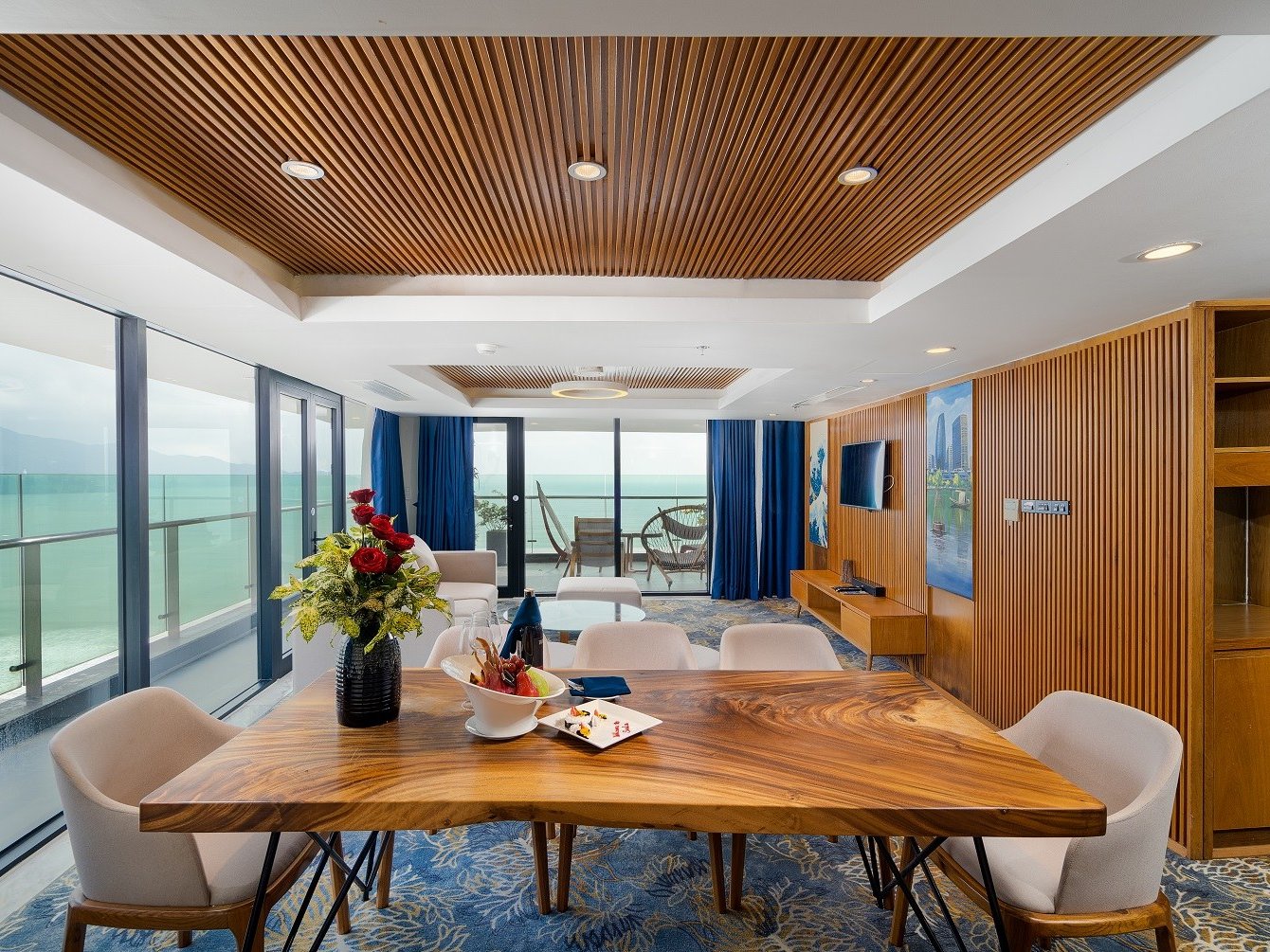 Suite living and dining room with a long wooden table and glass doors onto a sea-view balcony